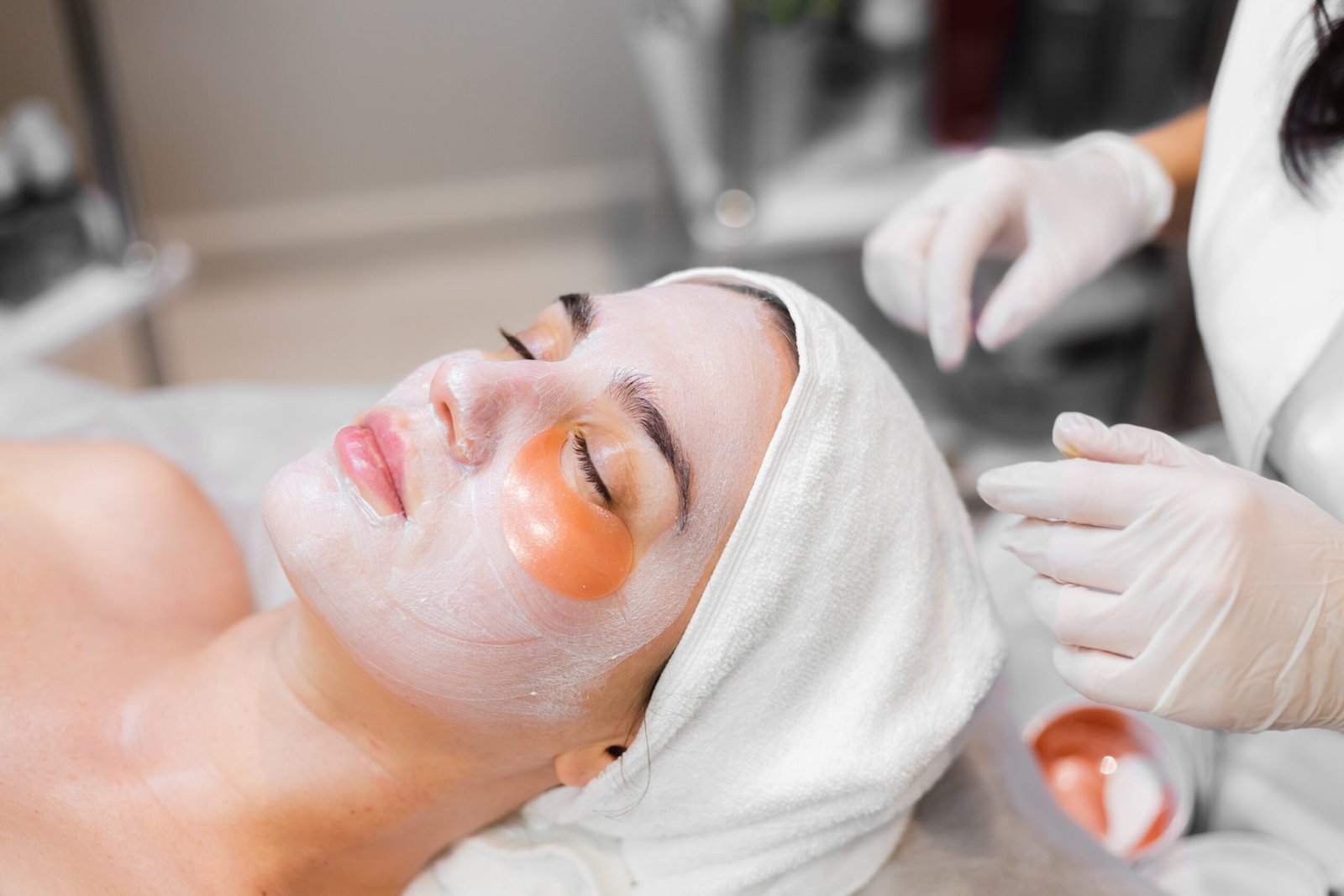 A young girl in a beauty salon in a cosmetology room lies on a bed relaxes with a mask on her face and patches under her eyes